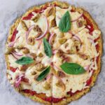 cooked cauliflower pizza crust with mozzarella cheese, sliced red onions, green olives, tomato sauce and fresh basil