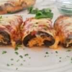 front view of 3 eggplant rollatini stuffed with ricotta, topped with mozzarella and garnished with parsley