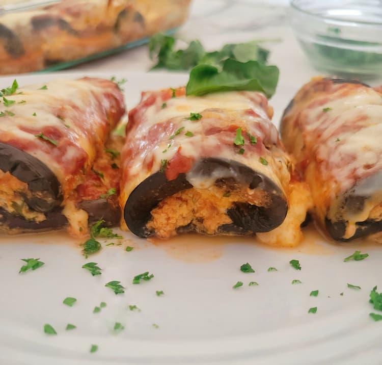 front view of 3 eggplant rollatini stuffed with ricotta, topped with mozzarella and garnished with parsley