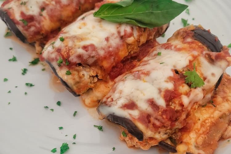 side view of 3 eggplant rollatini on a plate garnished with chopped parsley and a basil leaf