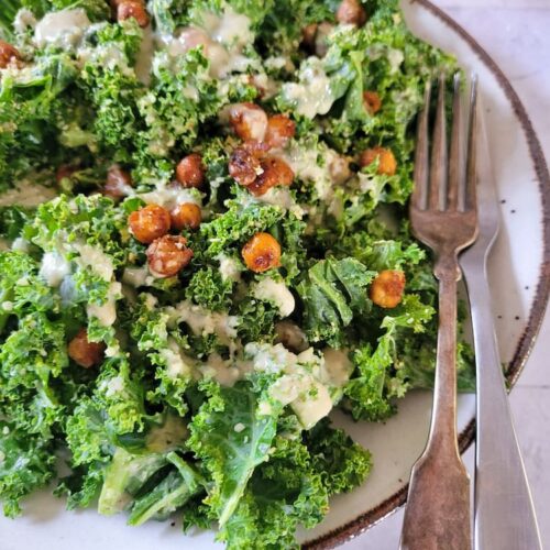plate of kale caesar salad with roasted chickpeas and a creamy dressing, lemon in the background, 2 forks on the plate