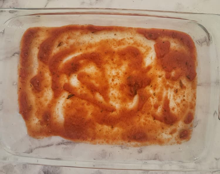 glass baking dish with tomato sauce spread in an even layer on the bottom