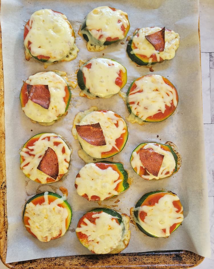 parchment lined baking sheet with cooked zucchini pizza bites, all topped with tomato sauce and mozzarella cheese and a few with pepperoni slices
