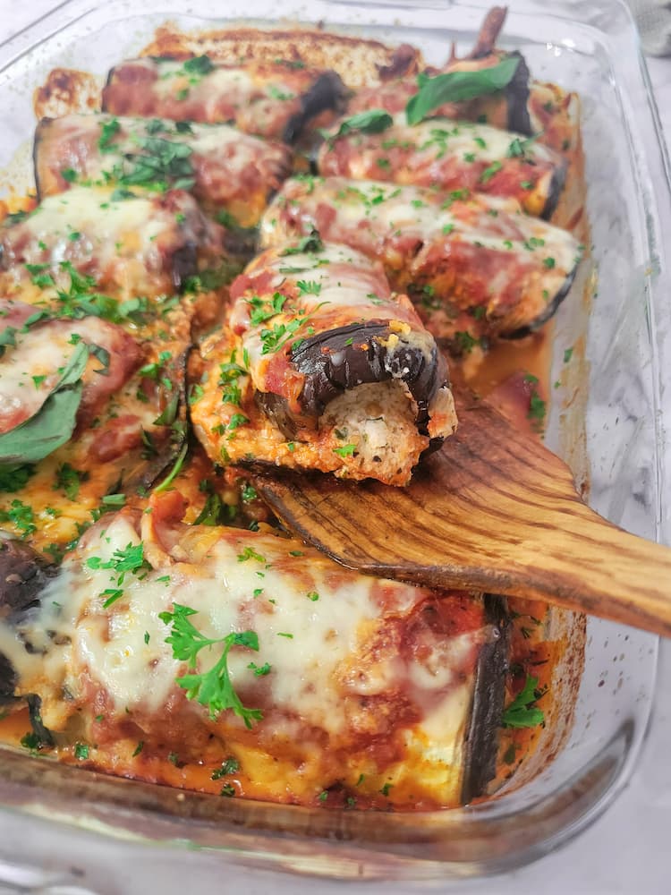 wooden spatula lifting up an eggplant rollatini out of a baking dish with the rest