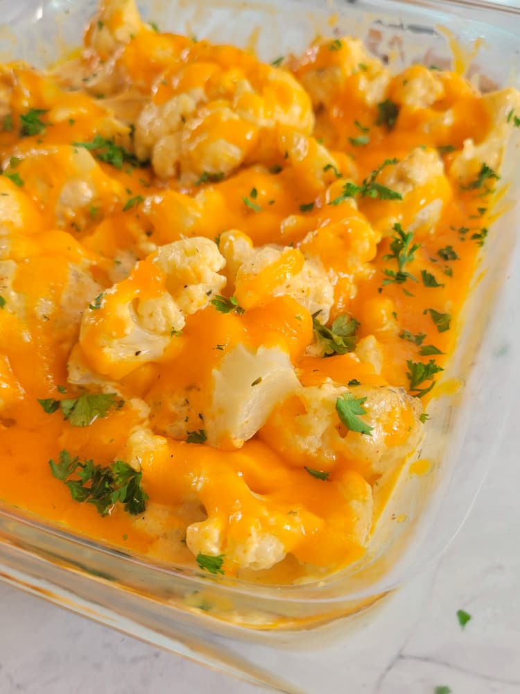 cauliflower mac and cheese in a glass casserole dish garnished with fresh chopped parsley