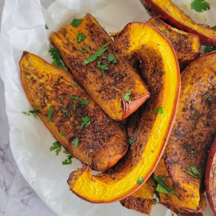 roasted and seasoned pumpkin wedges on a parchment lined plate, garnished with cilantro