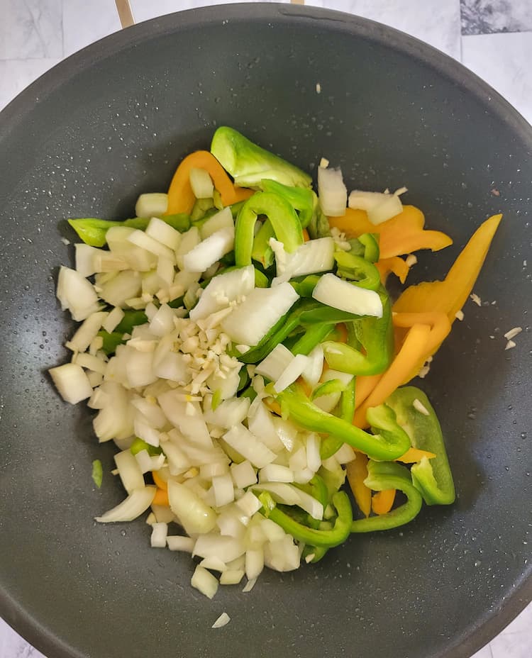 wok with raw diced white onion, minced garlic and sliced yellow and green peppers