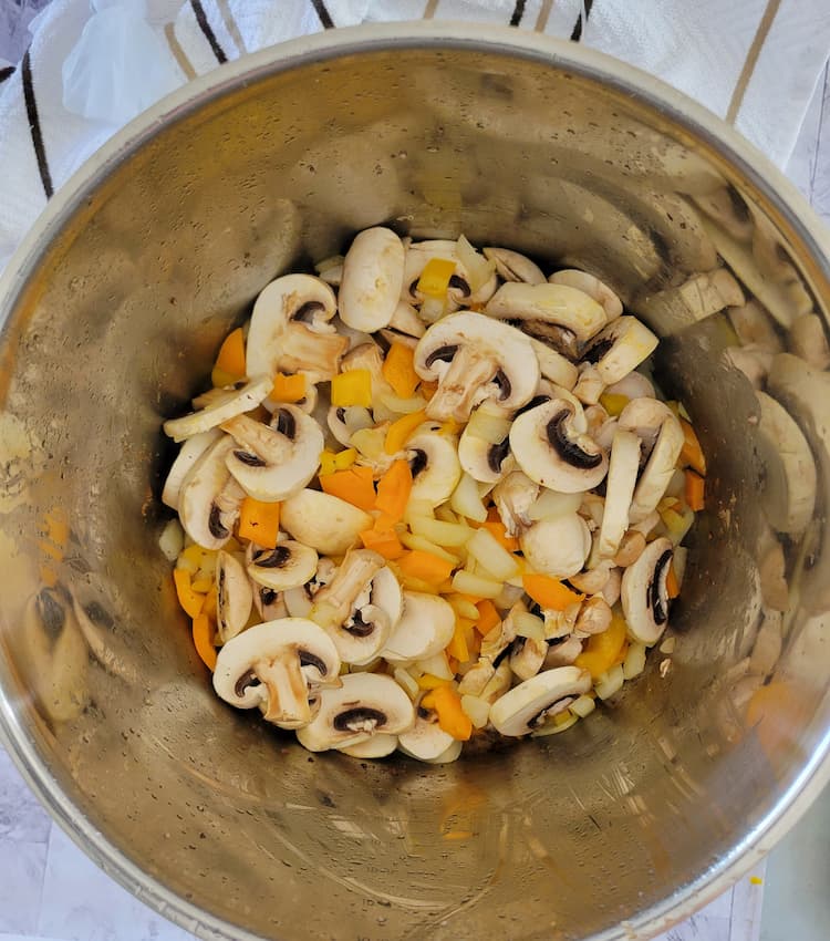 pot of sliced mushrooms, diced white onions and diced yellow and orange peppers