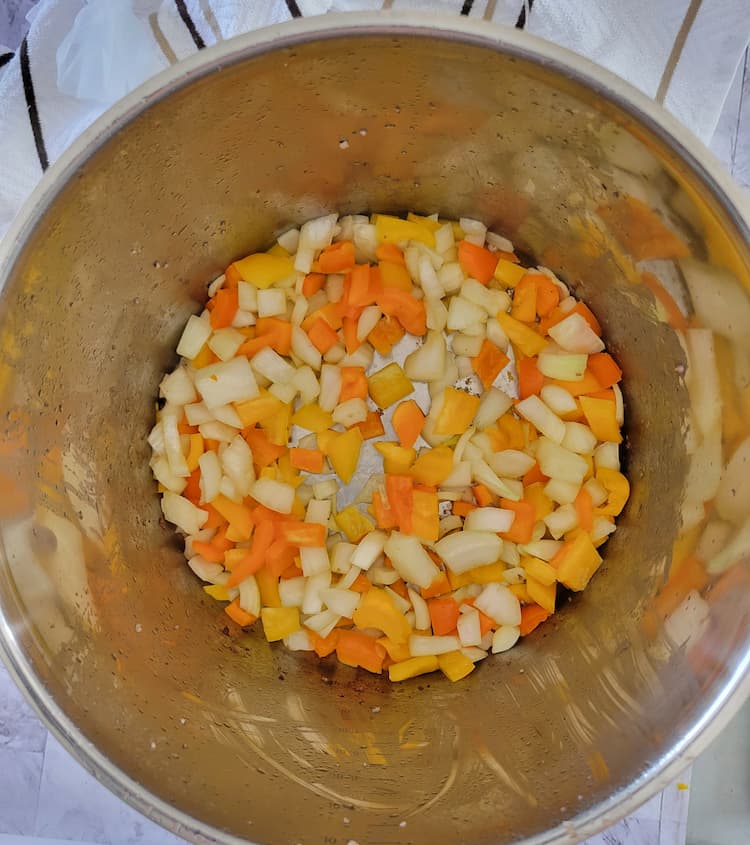 large pot with diced white onion and yellow and orange peppers satuéeing