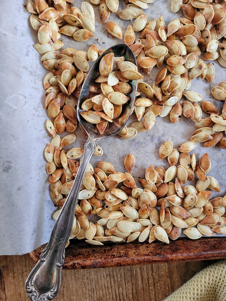 parchment lined sheet pan with whole roasted pumpkin seeds, spoon on the pan