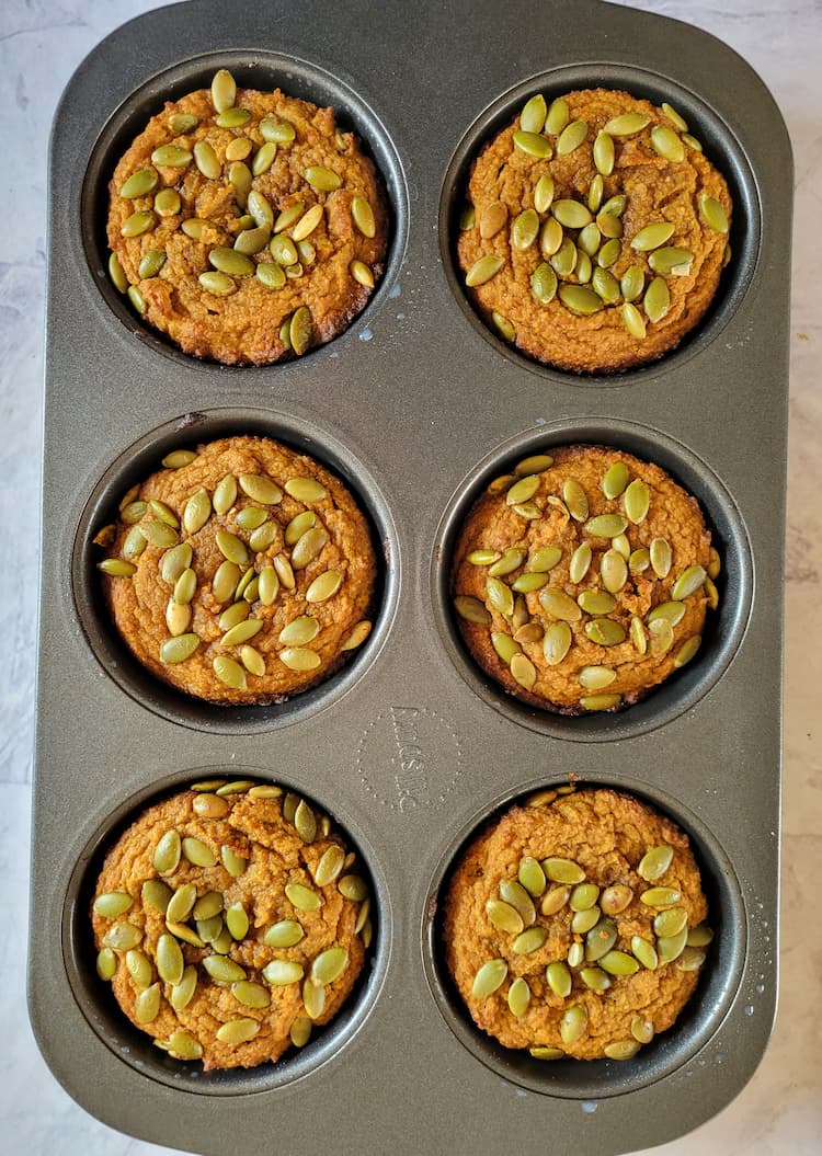 muffin tin with 6 freshly baked pumpkin muffins topped with pumpkin seeds