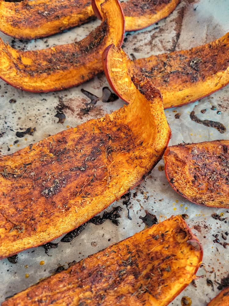side view of roasted pumpkin wedges on a parchment lined baking sheet