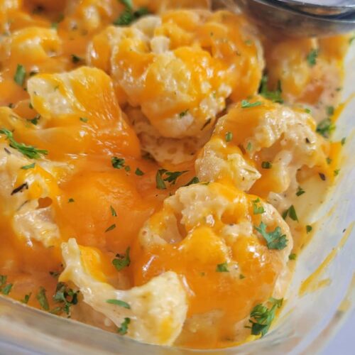 close up of cheesy cauliflower garnished with fresh chopped parsley, two spoons in the background