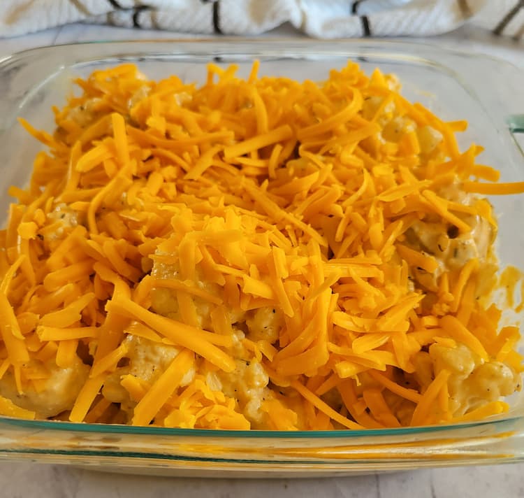 shredded cheddar cheese and cauliflower florets in a glass baking dish