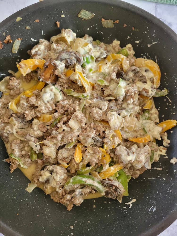 skillet with cooked sliced yellow and green peppers, ground beef, diced onions in a creamy white sauce