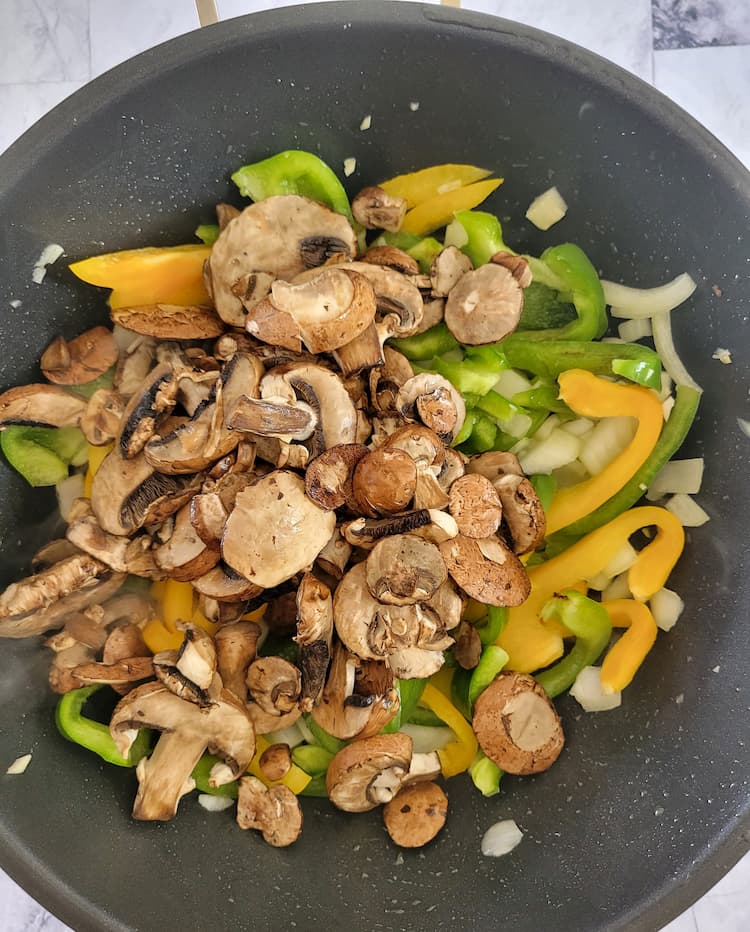 wok with sliced mushrooms, green and yellow bell peppers and onions