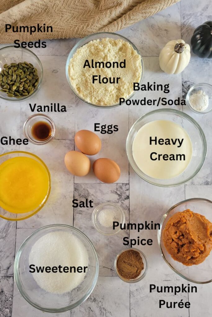 ingredients for easy recipe for pumpkin muffins - pumpkin puree, pumpkin spice, pumpkin seeds, almond flour, baking soda, baking powder, eggs, heavy cream, vanilla, ghee, sweetener, salt