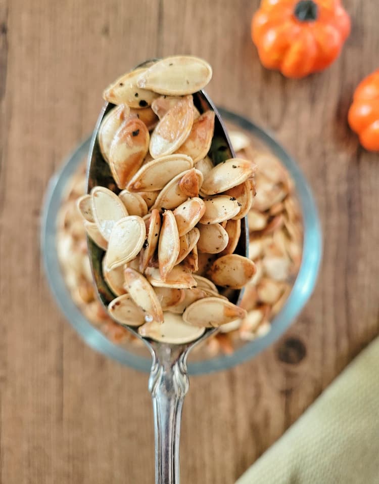 spoonful of whole roasted pumpkin seeds over a bowl of the rest, small pumpkins in the background
