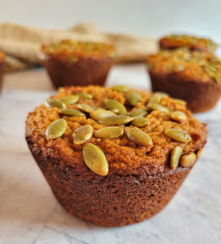 close up of a pumpkin muffin with pumpkin seeds on top, more muffins in the background