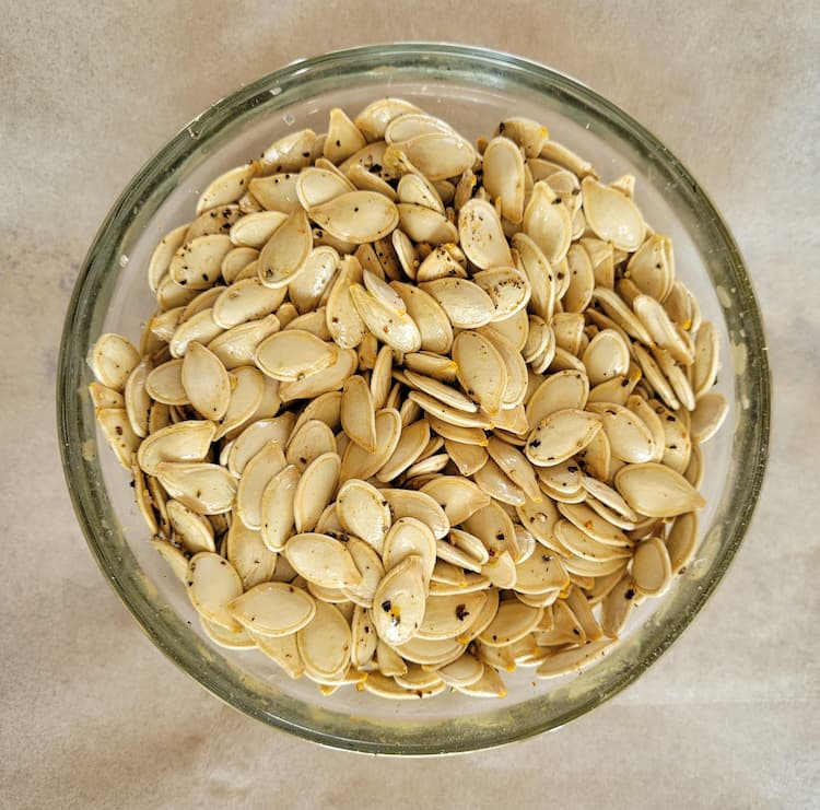 bowl of whole raw pumpkin seeds seasoned with salt and pepper