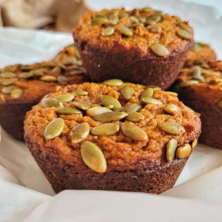 pumpkin muffins topped with pumpkin seeds stacked on a parchment lined plate
