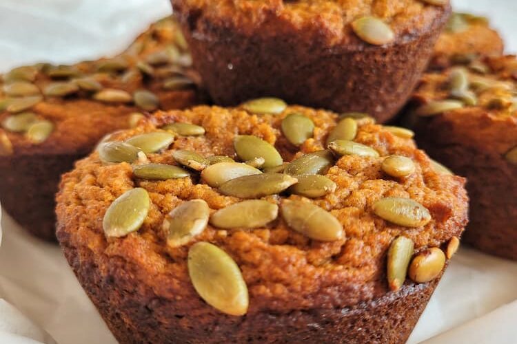 pumpkin muffins topped with pumpkin seeds stacked on a parchment lined plate
