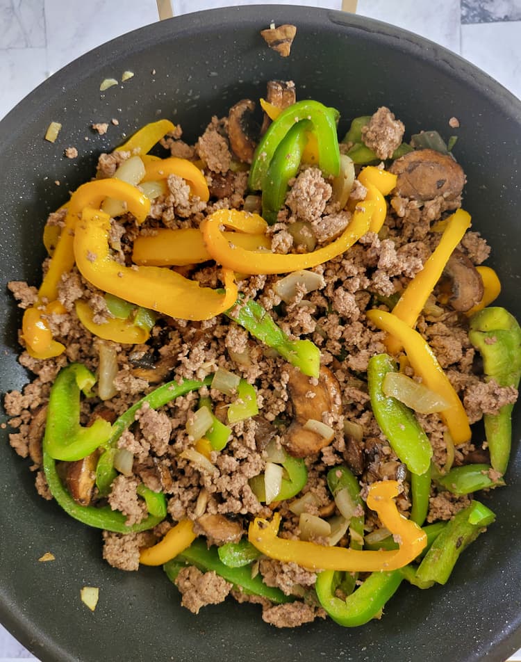 wok with cooked ground beef, diced onion and sliced yellow and green bell peppers