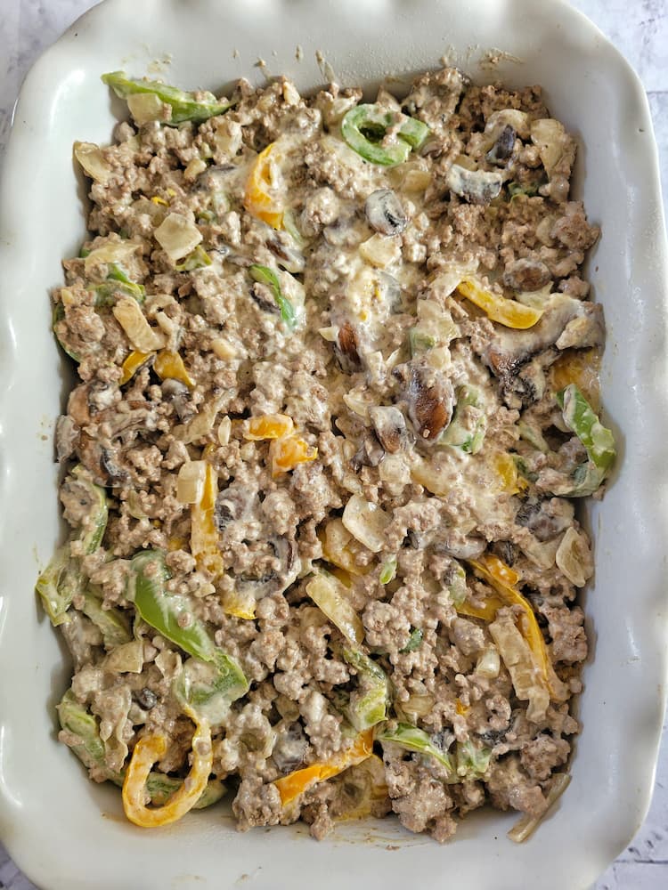 white glass casserole dish with cooked ground beef and sliced yellow and green peppers in a creamy white sauce