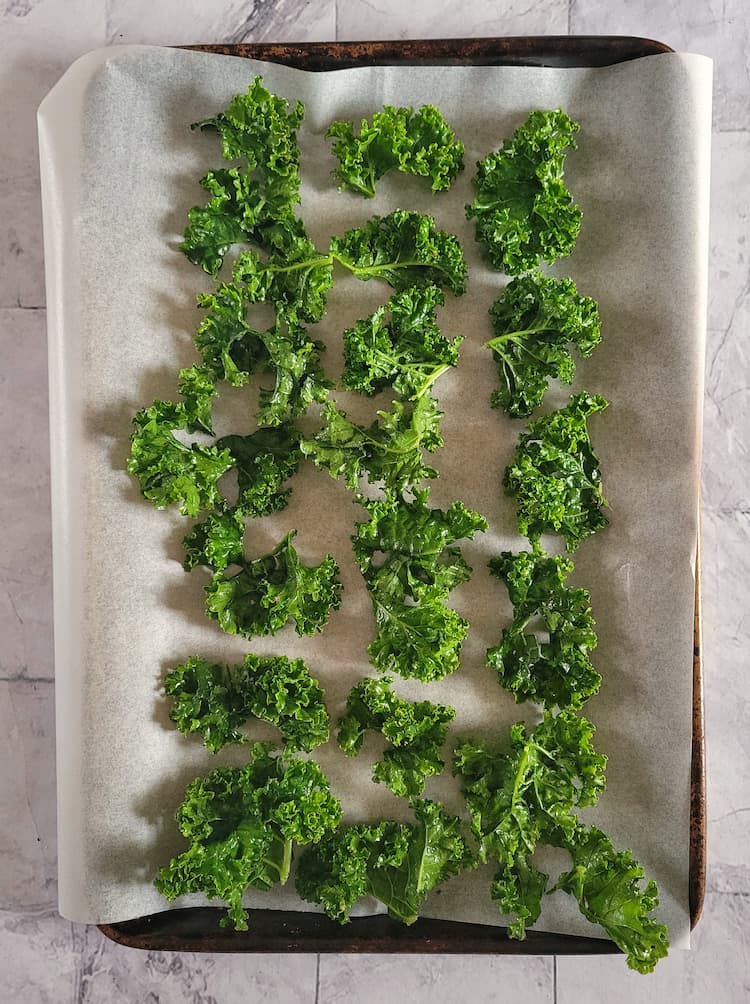 parchment lined baking sheet with pieces of kale spread out into a single layer