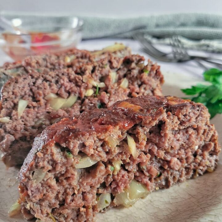 close up of slices of meatloaf on a plate, bowl of sauce next to forks in the background