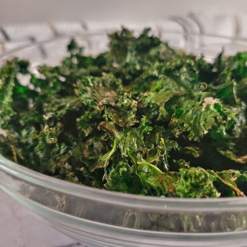 side view of a bowl of crispy seasoned kale chips.