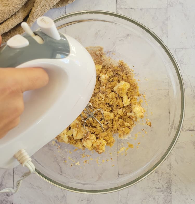 hand with an electric mixer mixed a bowl of ingredients like butter, cinnamon and sugar