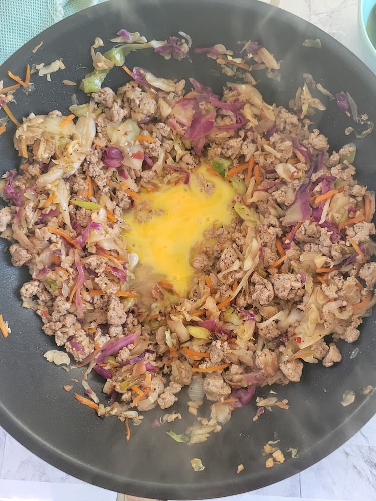 skillet with ground turkey and coleslaw with a well and raw egg yolk in the middle