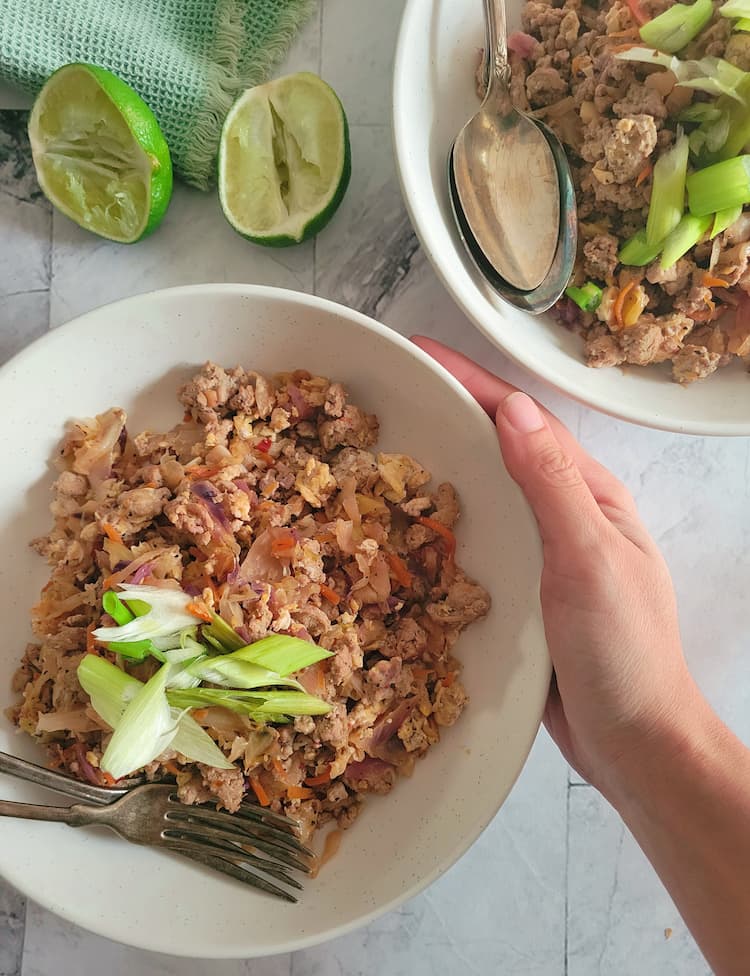 hand holding a bowl of ground turkey topped with green onions, two limes and another bowl of the same thing in the background