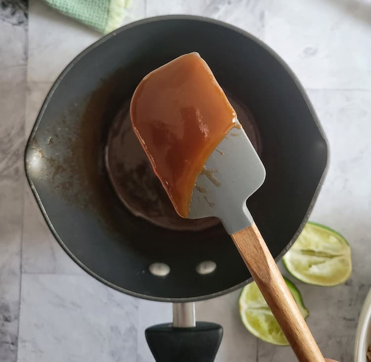 saucepan with a small rubber spatula coated in a red thick sauce, two limes in the background
