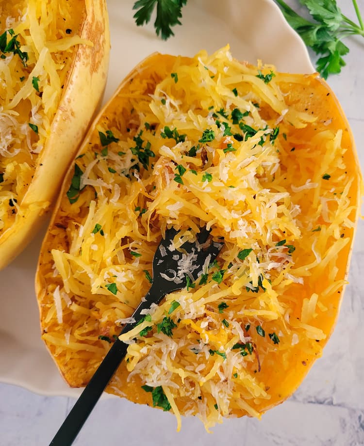 two cooked spaghetti squash halves with parmesan and parsley, fork in one half