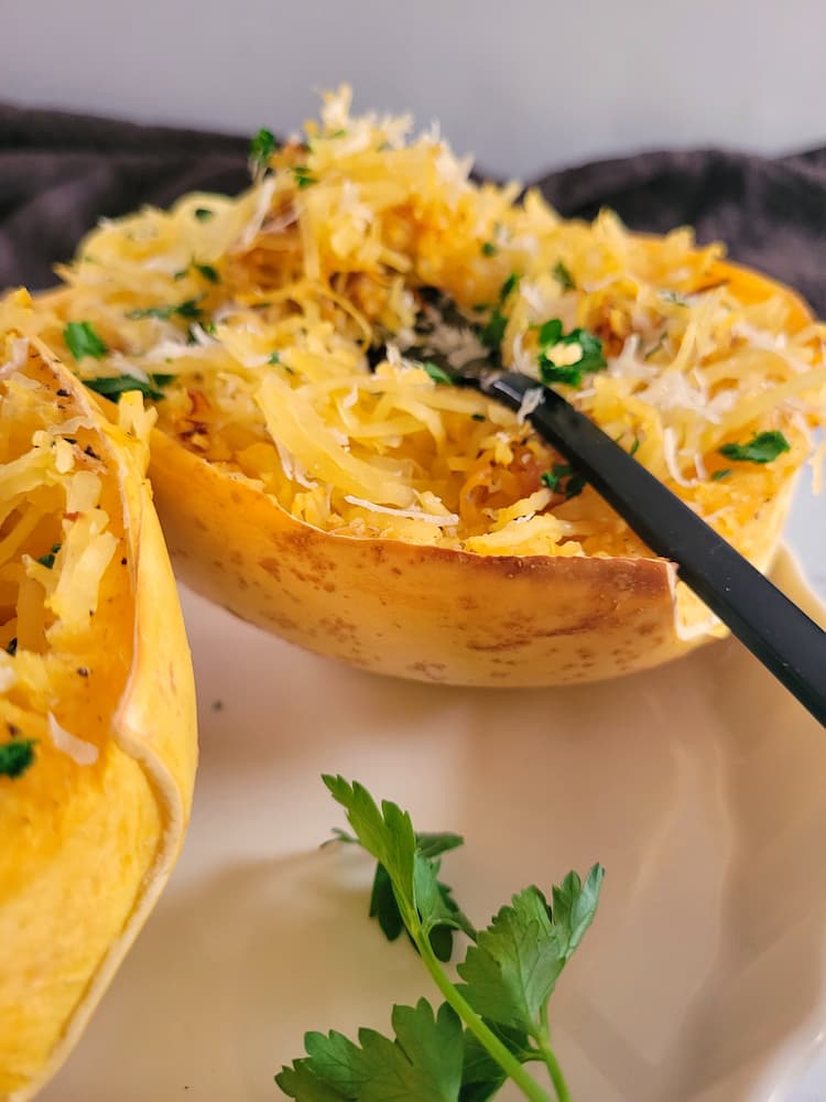 side view of a fork in a cooked spaghetti squash half garnished with parsley and parmesan