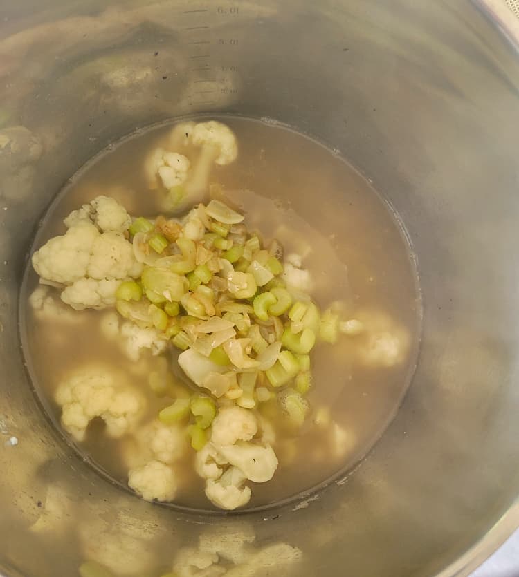 pot of cauliflower florets, celery and onions in chicken broth and water