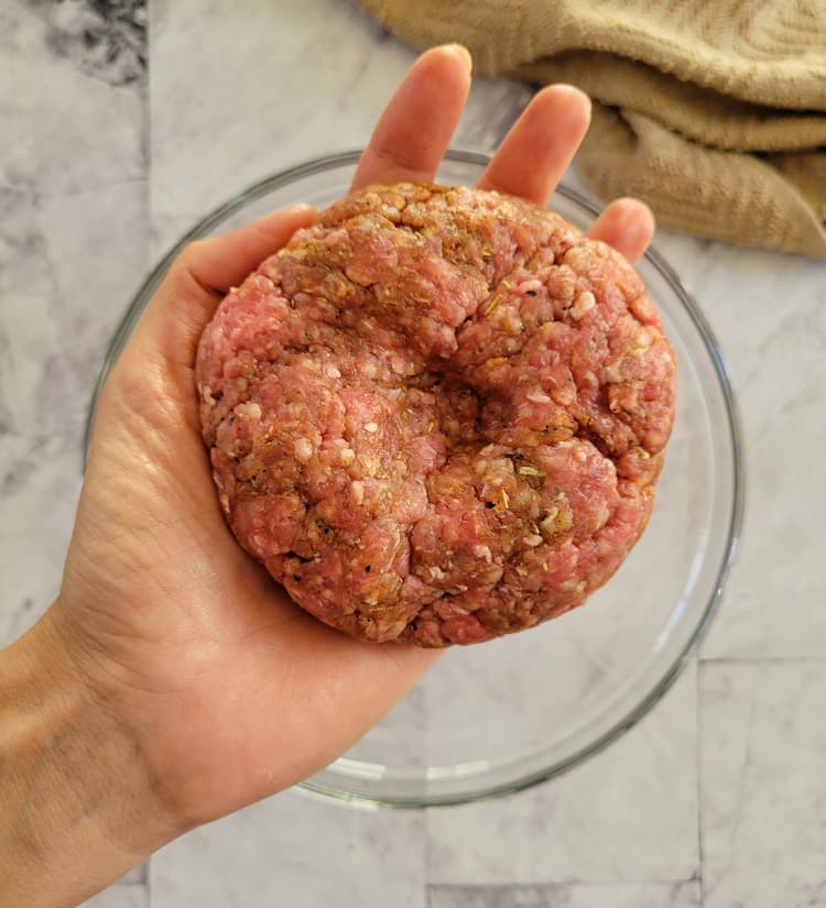 raw beef burger with a dimple in the center in the palm of a hand