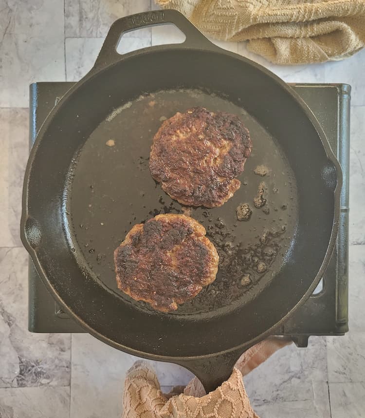 two cooked beef patties in a black cast iron skillet