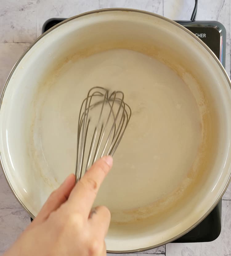 hand with a whisk whisking a milky coloured liquid in a pot