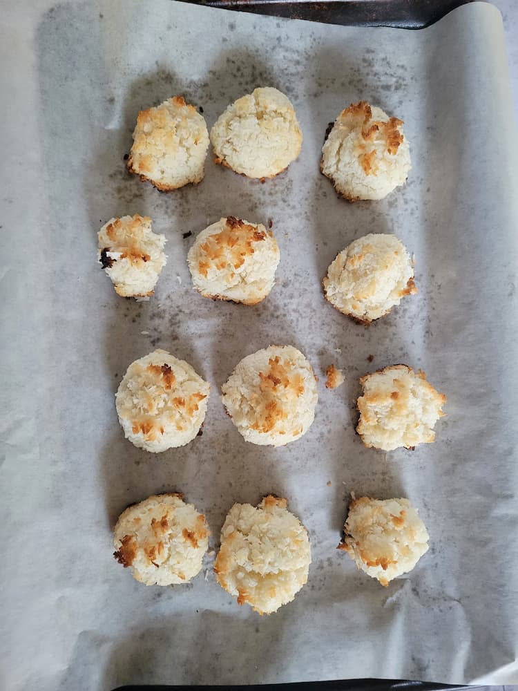 12 freshly baked gluten free macaroons (coconut) on a parchment lined baking sheet