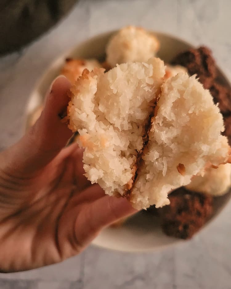 hand holding a coconut macaroon split in half up to the camera above a plate with more and chocolate versions in the background