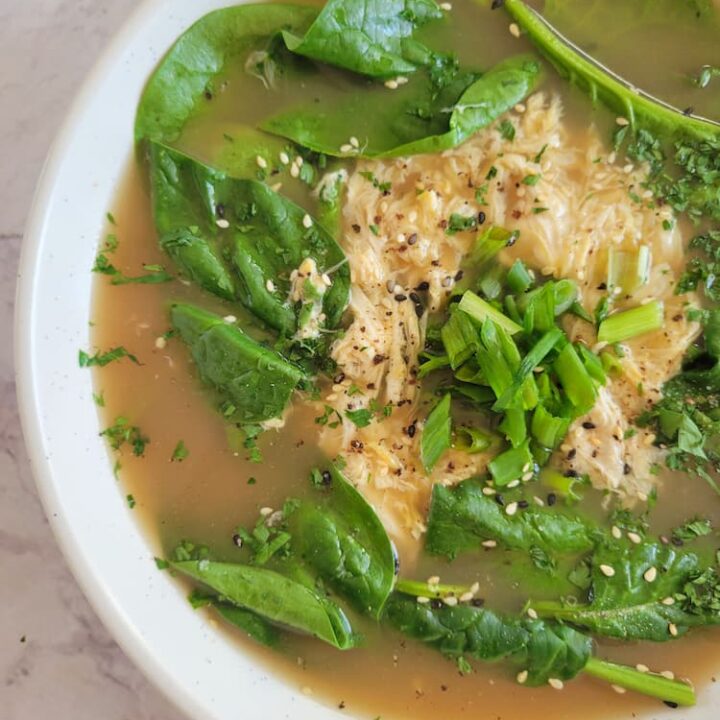 close up of egg drop soup in a bowl with broth, spinach, eggs, parsley, sesame seeds