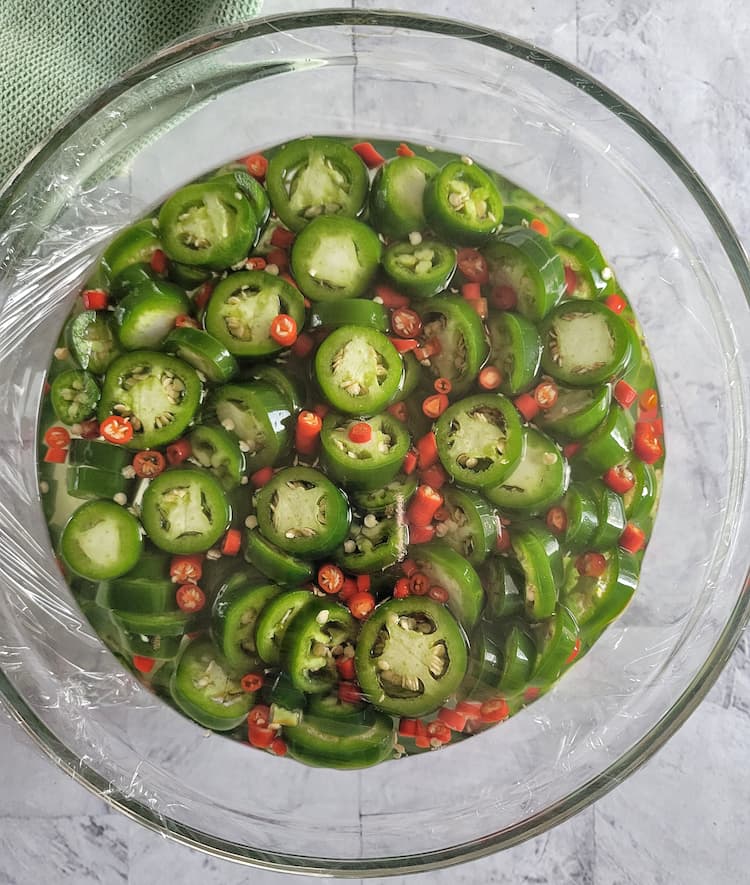 bowl of sliced jalapeños and thai red chilies in vinegar, siran wrap over the bowl