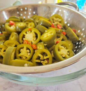 colander with sliced jalapeños and red thai chilies