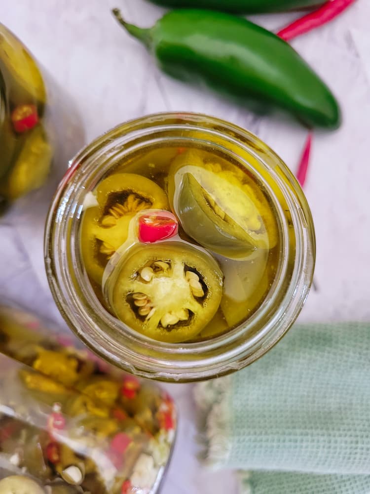 jar of sliced jalapeños and thai red chilies in olive oil, more peppers in the background