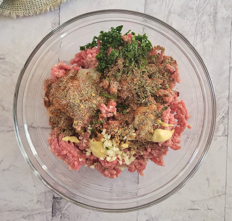 bowl of raw ground beef with spices, dijon mustard, minced garlic, chopped parsley