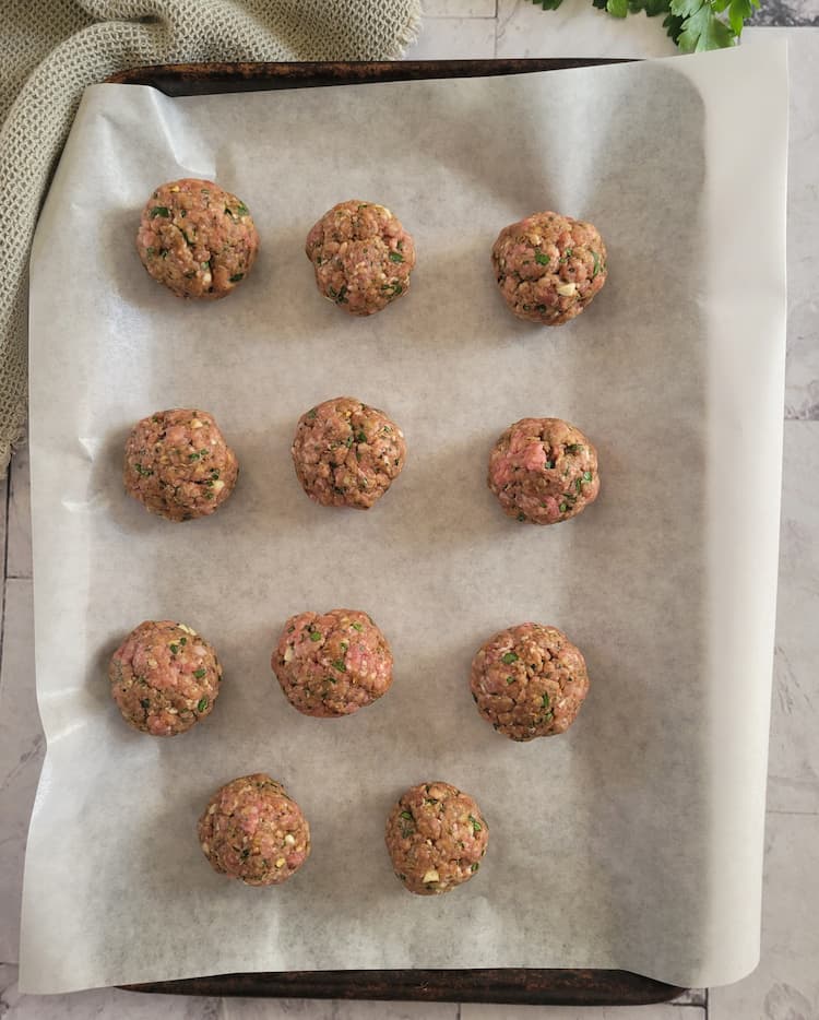 11 raw gluten free meatballs on a parchment lined baking sheet