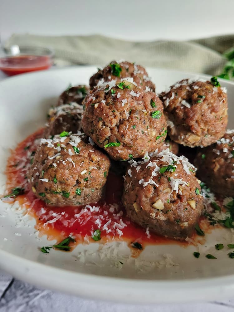 a bowl of gluten free meatballs garnished with parsley, bowl of sauce in the background